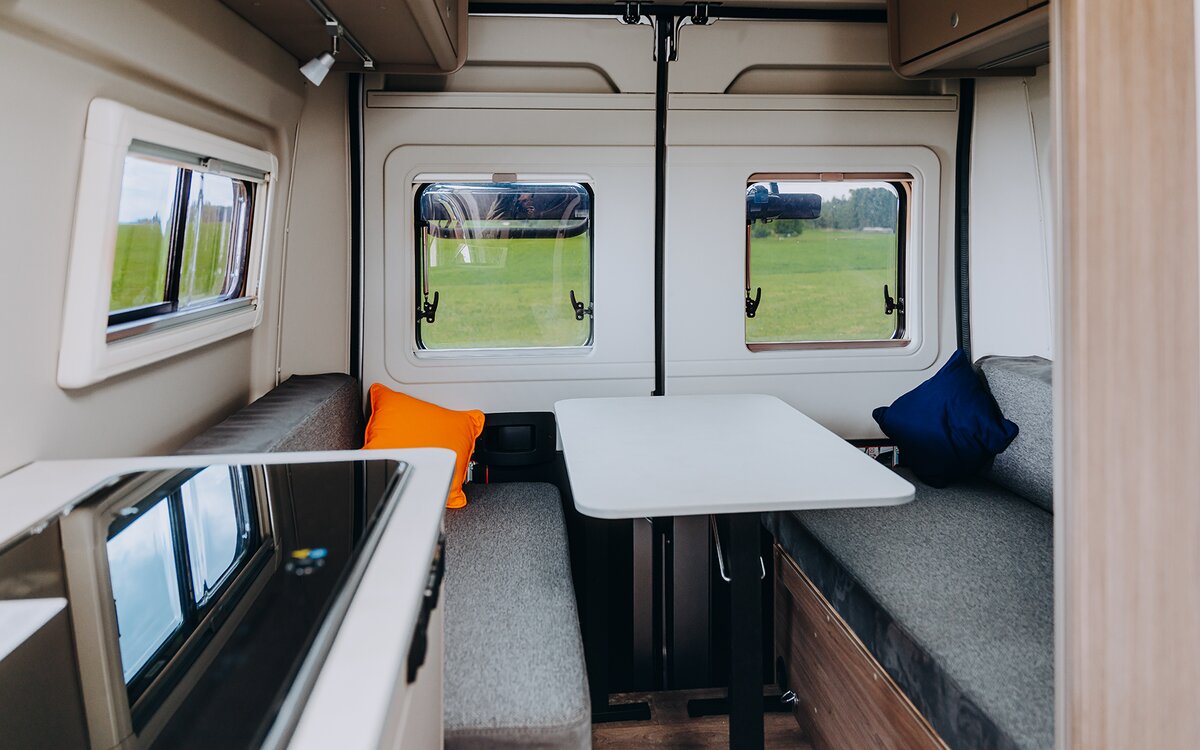 Seating area in the Carado motorhome with a table, two upholstered benches, windows and overhead cabinets