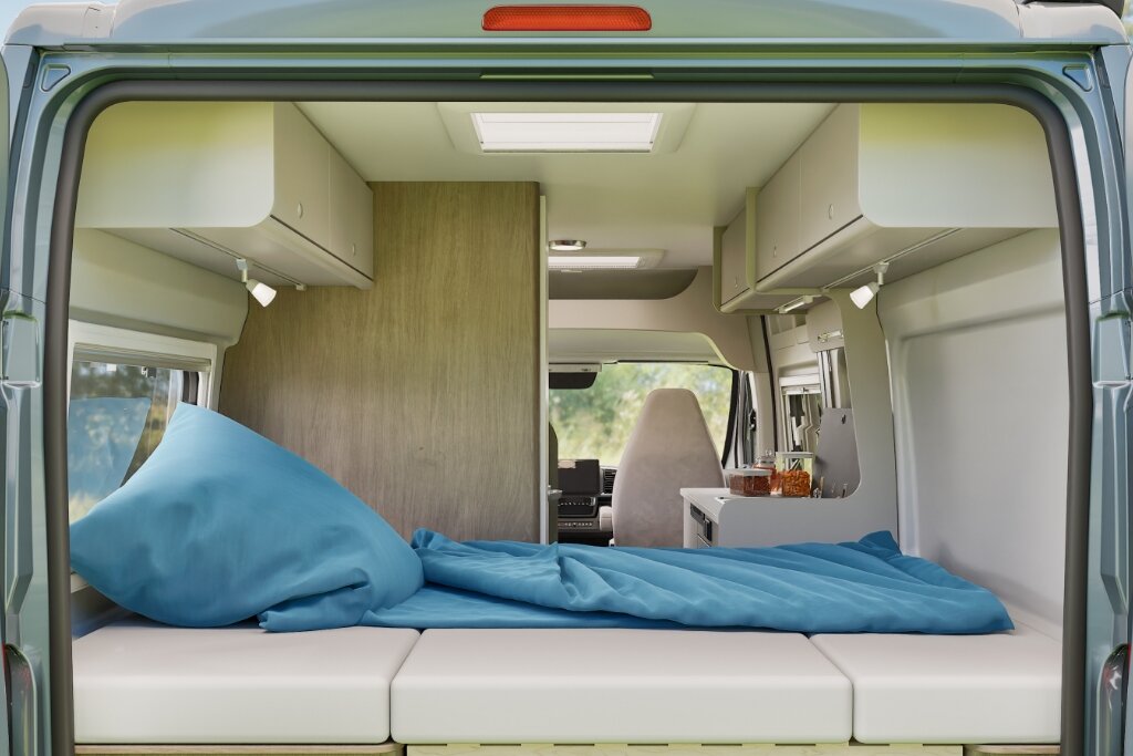 Rear bed in a Carado motorhome with blue bedding, view from the rear through the interior to the kitchen