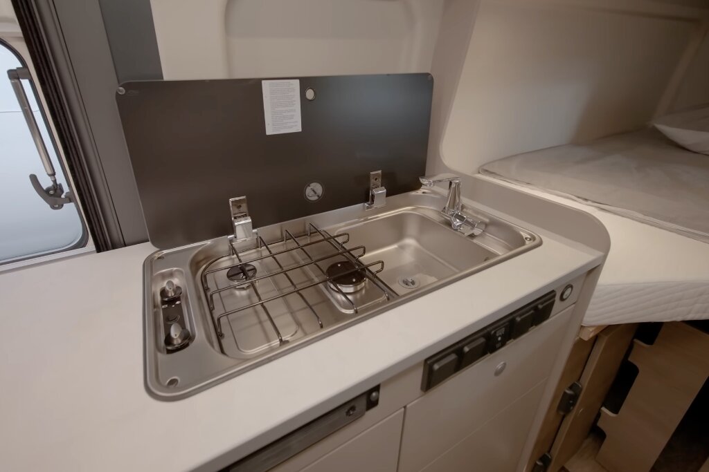 Kitchen unit in the Carado motorhome with a two-burner gas hob, sink and glass cover next to the bed
