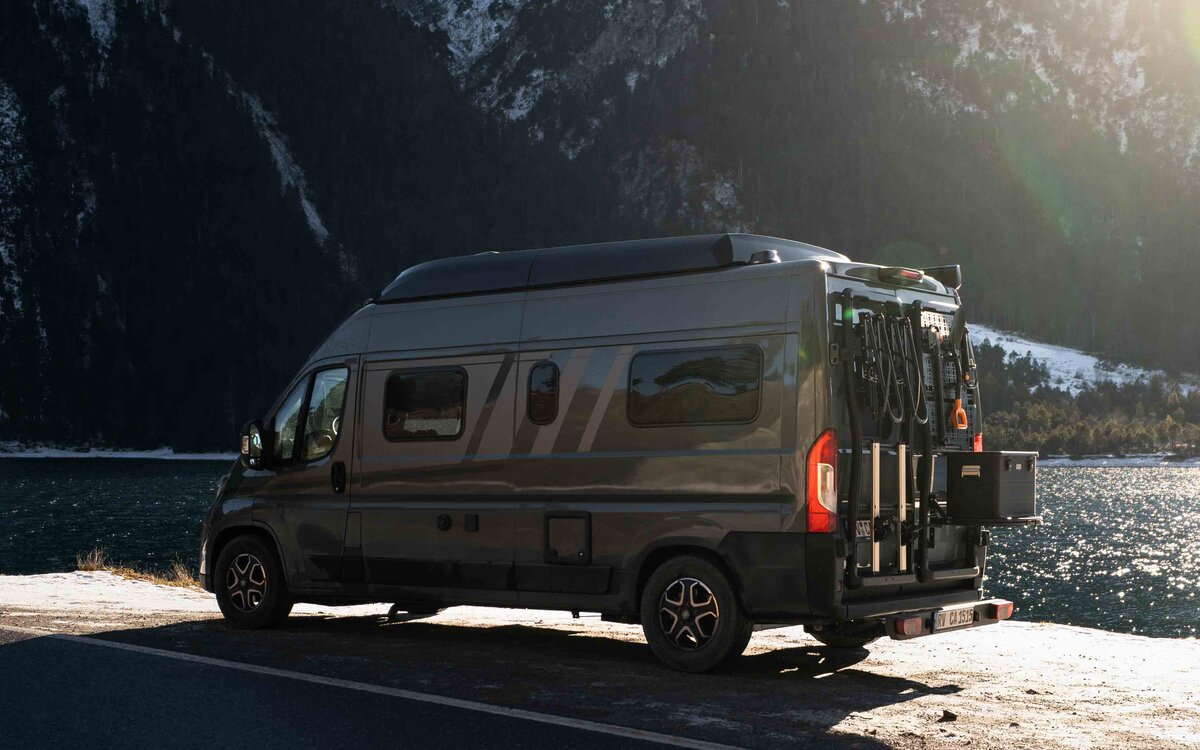 Carado motorhome on the lakeshore in front of snow-covered mountains, side view with rear bike rack