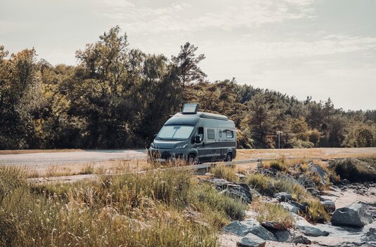 Carado motorhome parked by the roadside near a rocky shoreline and trees, front and side view