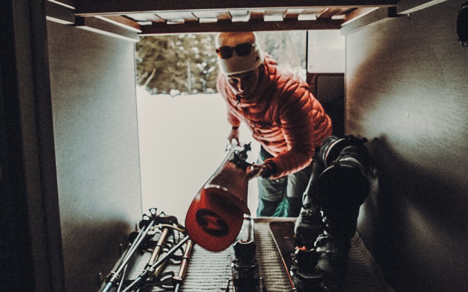 View into the rear garage of a Carado motorhome with skis, poles and ski boots; a person is loading winter sports equipment.