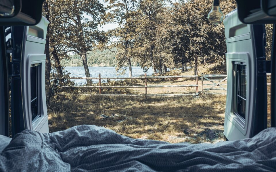 View from the Carado motorhome bed onto trees, a fence and the lake at the pitch