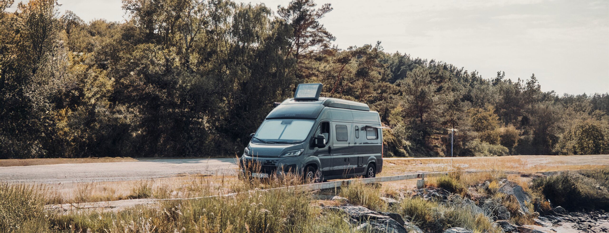 Carado motorhome parked by the roadside in a coastal landscape with rocks and trees