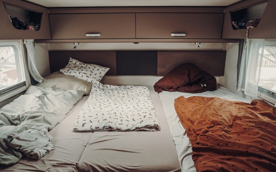 Sleeping area in the Carado motorhome with double bed, overhead cabinets and side windows