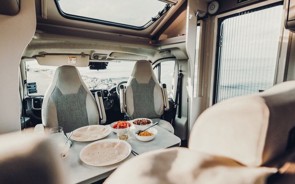 Carado motorhome interior with a seating area, a laid table and swivelling front seats