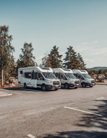 Three Carado motorhomes parked at the edge of a forest, shown from the front and the side