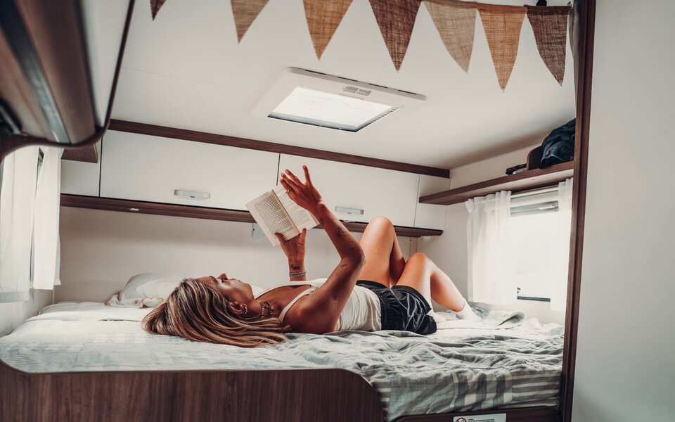 A woman reads on the bed inside a Carado motorhome