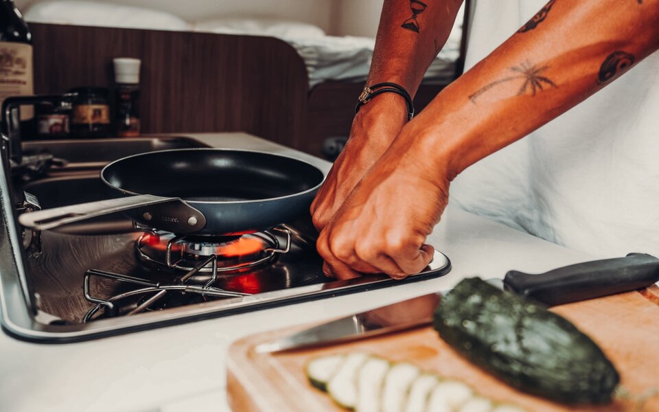 Person cooking on the gas stove in the kitchen of a Carado motorhome, with pan, sink, and cutting board