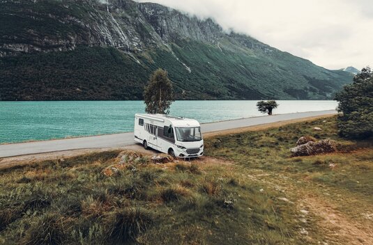 Carado motorhome on the shore of a mountain lake, angled front view on a meadow beside the road