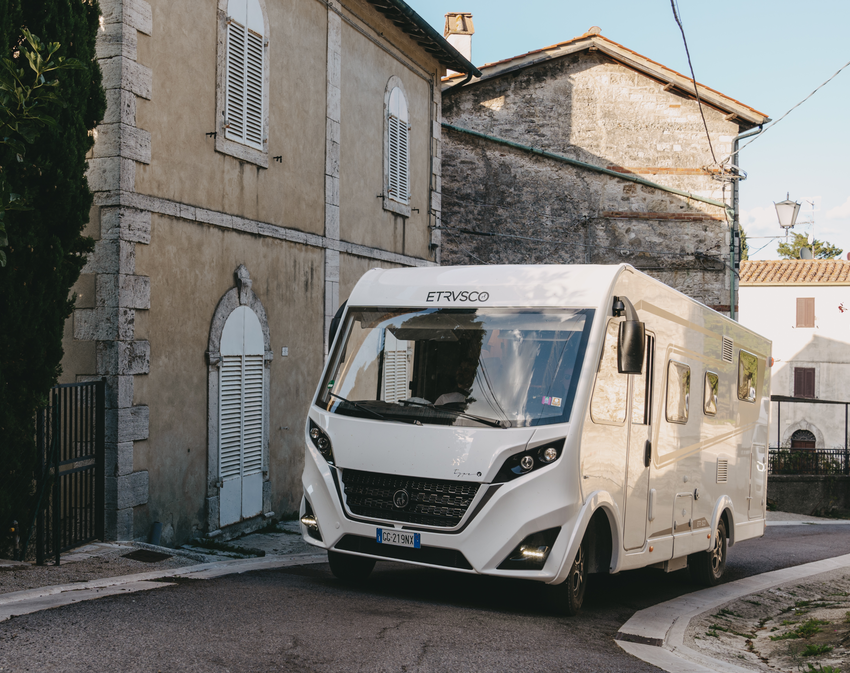 Ein Etrusco integriertes Wohnmobil fährt durch eine italienische Dorfstraße, umgeben von historischen, mediterranen Gebäuden.