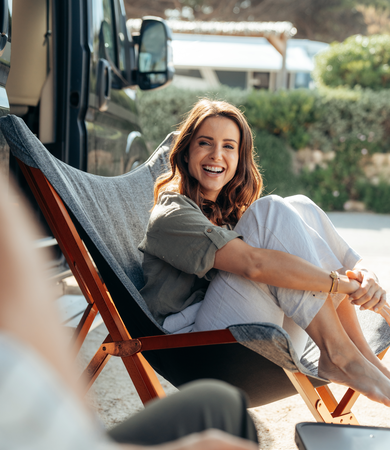 Smiling woman in a camping chair on a sunny campsite - Fiat campervan in the background.