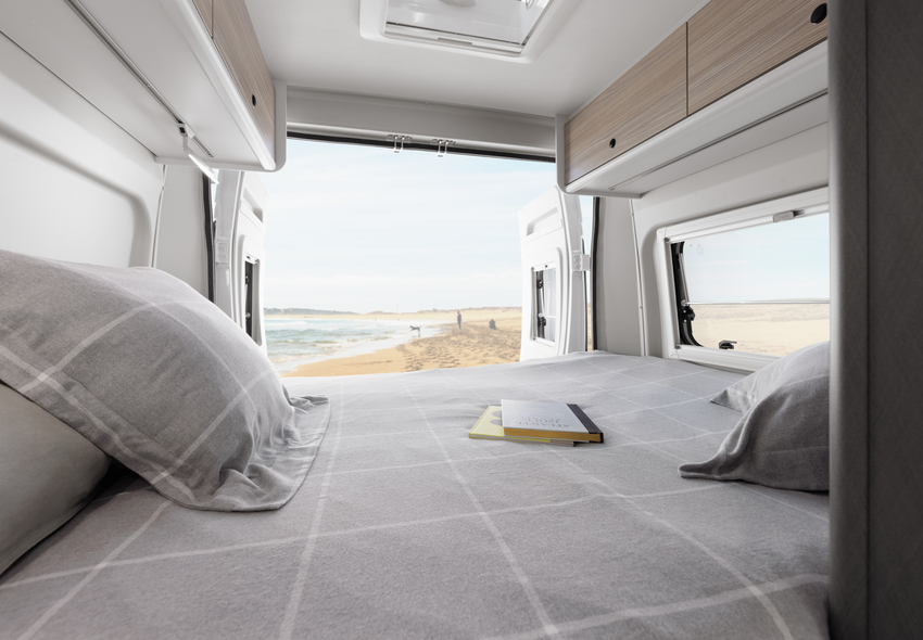 Modern interior of an Etrusco Campervan Fiat with living area, double bed, and coastal view through a large window - ideal for camping.