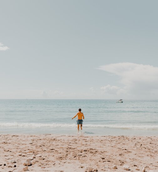 Man on the beach in a yellow T-shirt and blue shorts walking towards the sea during a relaxed camping trip.