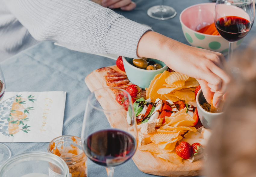 Camping meal with snacks, olives, strawberries, cheese, red wine, and a hand on the table, ideal for gathering while camping.