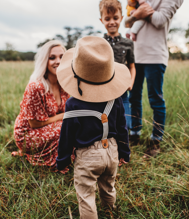 Family on a meadow enjoys nature during a camping trip – Child with straw hat runs to the mother, father and children in the background.