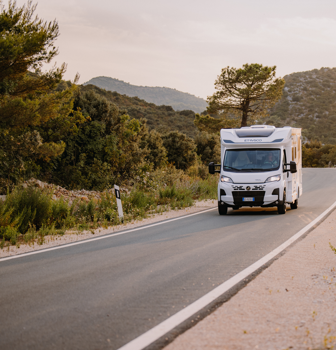 White Etrusco Fiat motorhome drives through an Italian city with colorful facades and an urban, relaxed atmosphere.