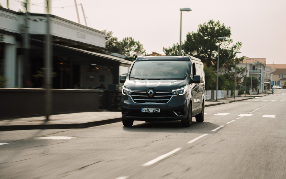 Etrusco Renault Urban Camper drives through an urban environment with modern architecture, perfect for camping and spontaneous city trips.