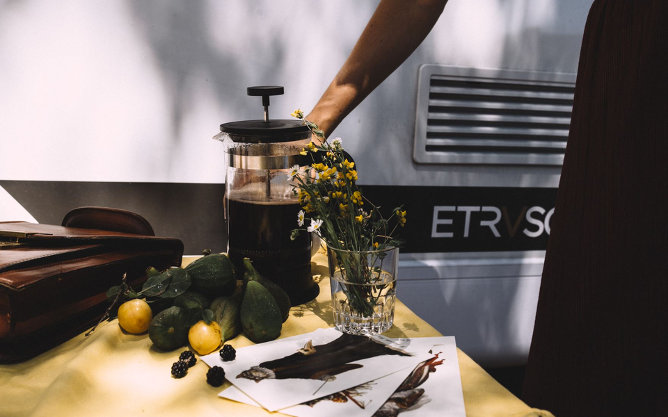 Campingscene med friske citroner, blomster og en kaffekande på et bord foran en Etrusco autocamper, ideel til afslappende øjeblikke.