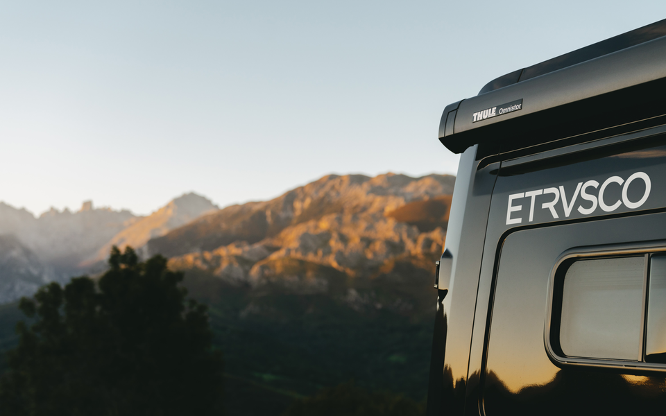 Baggudsigt af en Etrusco campervan foran en malerisk bjergkulisse ved solopgang, ideel til camping i naturen.