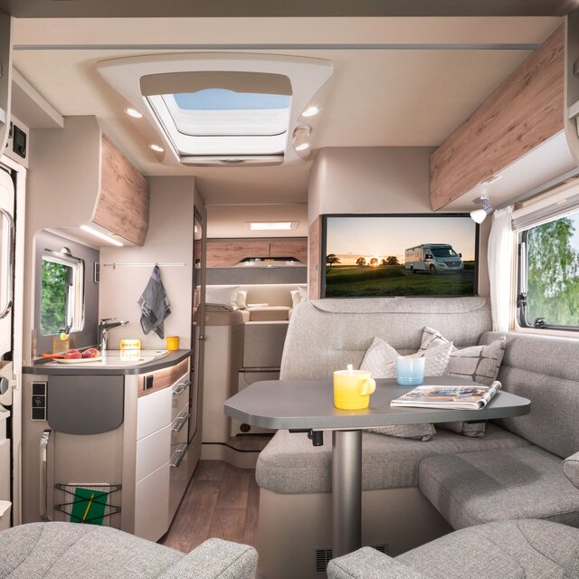 Bodel i HYMER Exsis-t 580 med soffgrupp och plasma-TV med bakgrundsbild, ingångsdörr, köksdel och sovdel