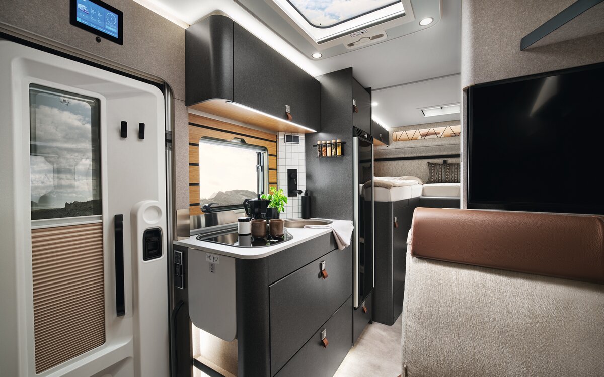 På spisen i HYMER ML-T i stilen Velvet Ash står en kastrull. Framför syns dörren och ovanför den HYMER Connect-displayen.
