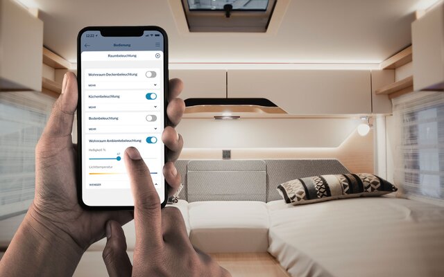 Händerna på en person som använder en mobiltelefon i sovområdet bak i en husbil, skärmen visar användningen av HYMER Connect-appen