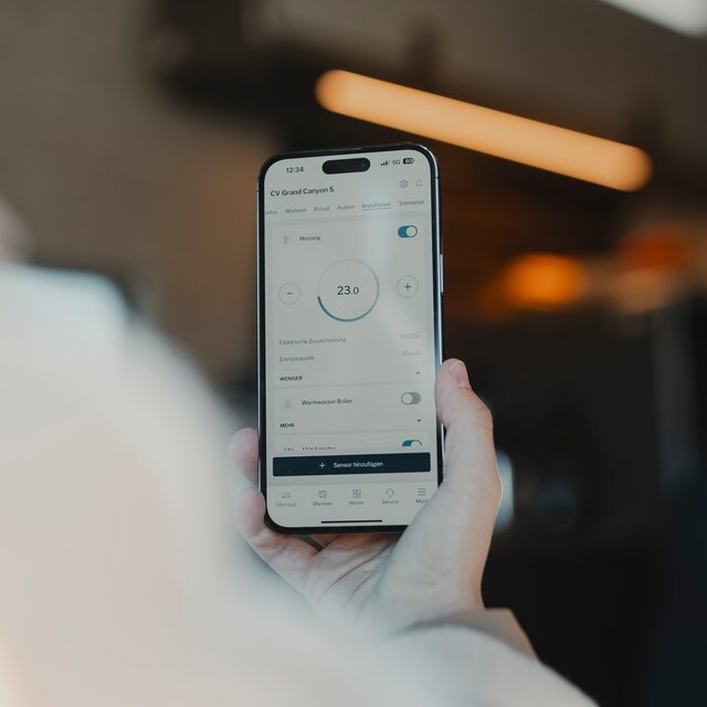 Person using the HYMER Smart Connect app on their mobile phone while sitting in a camper van