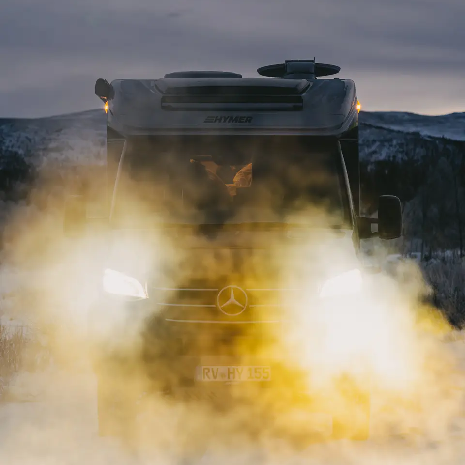Front view of the HYMER ML-T CrossOver with headlights on, vehicle standing in a snowy landscape, mountains with snow in the background