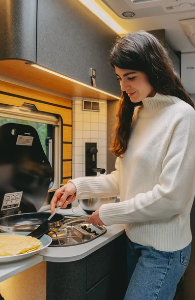Young woman preparing pancakes in the motorhome kitchen of a very modern motorhome