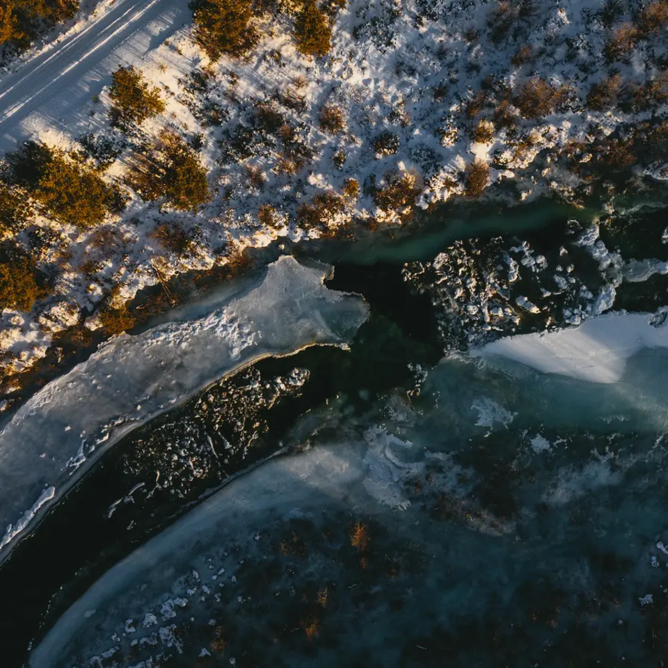 Aerial view of an almost frozen river, a snowy road next to it