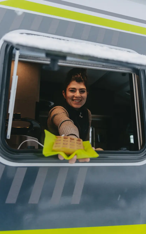 View into the kitchen window of the HYMER ML-T 570 CrossOver, a woman handing out a waffle