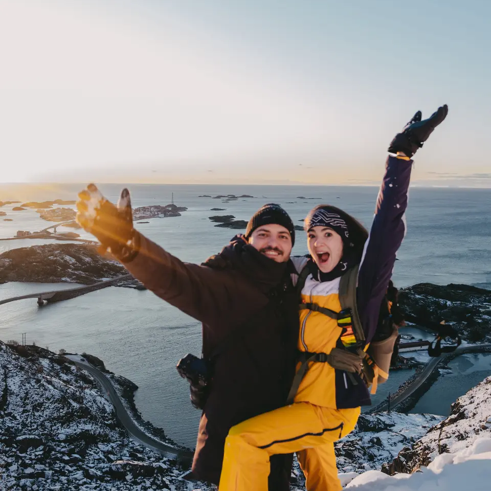 Man and woman at a viewpoint, snowy mountains and the sea in the background