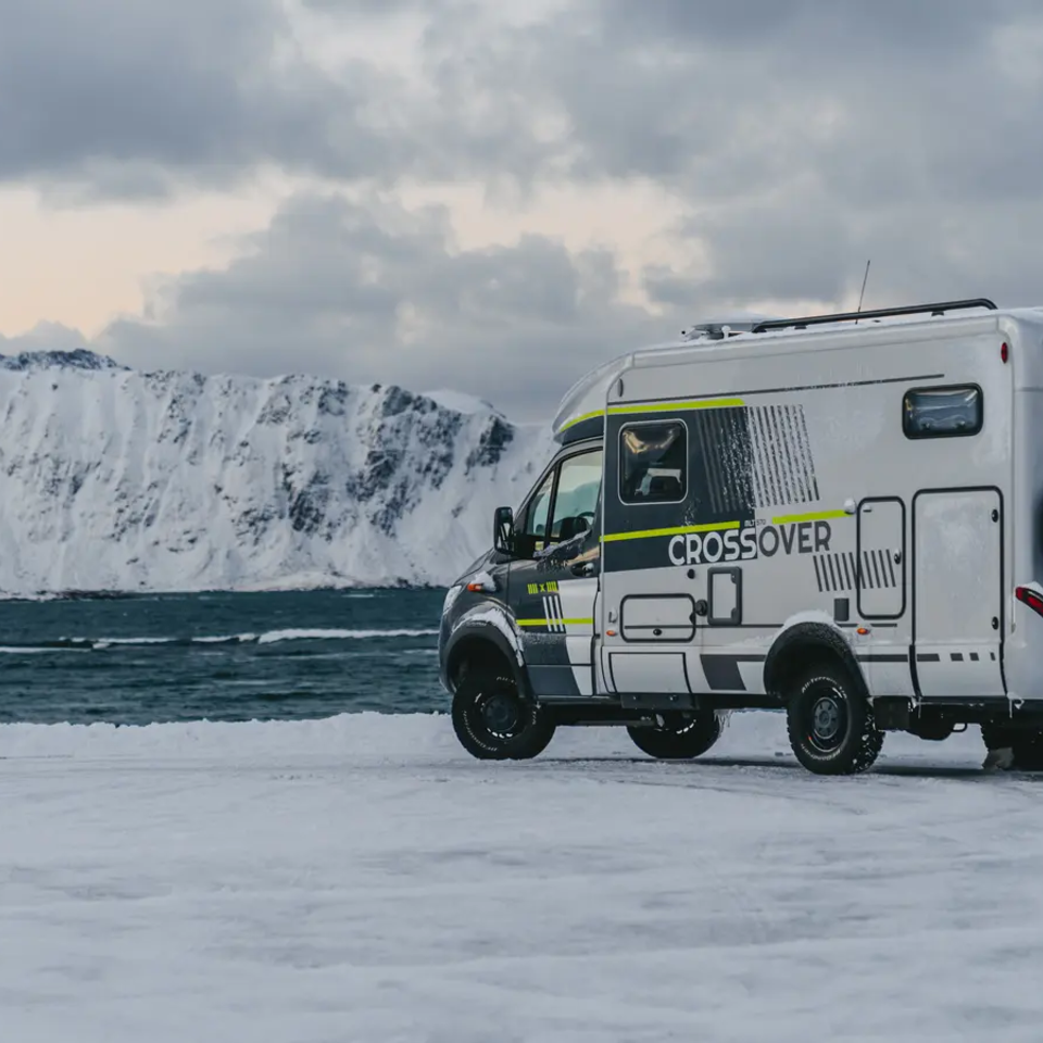 Side view of the HYMER ML-T 570 CrossOver, high snow-covered mountain and the sea in the background