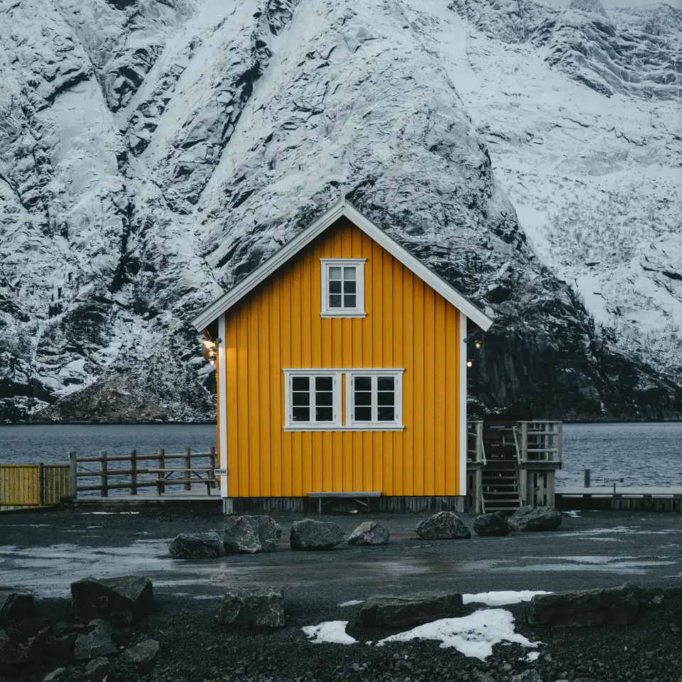 Yellow small house at the fjord, a large snow-covered mountain in the background